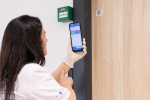 Profesional de Integra CEE utiliza un teléfono móvil para escanear un código QR situado junto a una puerta interior en un entorno corporativo, como parte de las funciones de control de tareas y gestión digital de instalaciones.