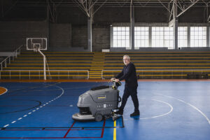 Trabajador de Integra CEE utiliza una máquina fregadora para la limpieza del pavimento de una pista deportiva interior. 