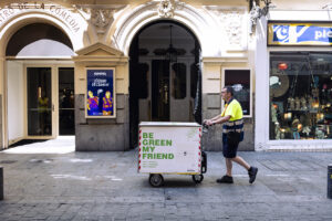 Servicio de última milla y logística urbana de Integra CEE Profesional de Integra CEE transporta un carro eléctrico de logística en una vía peatonal frente a un edificio cultural, como parte de un servicio de última milla y distribución sostenible.