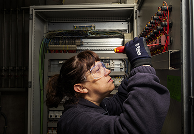 Una trabajadora de Integra CEE realiza tareas de mantenimiento eléctrico en un cuadro de control, utilizando herramientas y equipos de protección individual. 