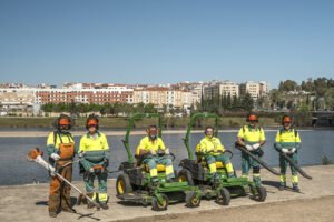 Un equipo de seis profesionales de Integra CEE posa con maquinaria especializada para la realización de trabajos medioambientales de zonas exteriores junto a un entorno fluvial urbano. 