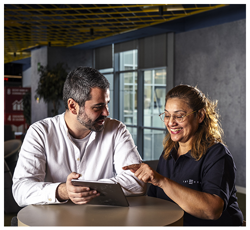 Integra_ACOMPANAMIENTO-Programas-desarrollo_ProgramadeAtencionSociolaboralEspecializada_500x460px Técnico de apoyo y trabajadora de Integra CEE en una sesión de acompañamiento sociolaboral. Las dos personas se encuentran sentadas alrededor de una mesa alta redonda en el interior de un espacio moderno de oficinas.