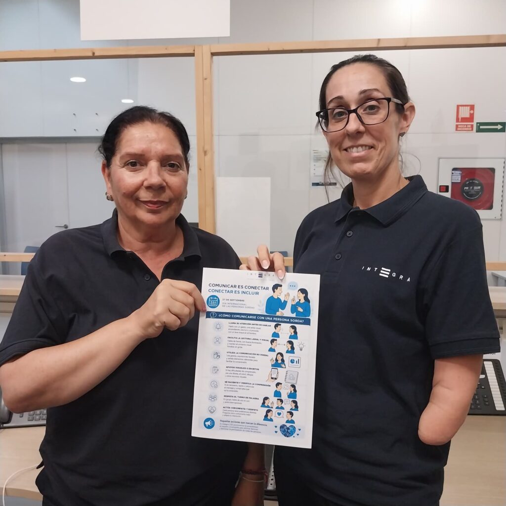 Dos personas trabajadoras de Integra CEE muestran un cartel informativo de la campaña "Comunicar es conectar, conectar es incluir" en un entorno de oficina de la ciudad de Ceuta. El cartel reúne pautas para mejorar la comunicación con personas sordas, como favorecer la lectura labial, utilizar apoyos visuales y respetar los turnos de palabra.
